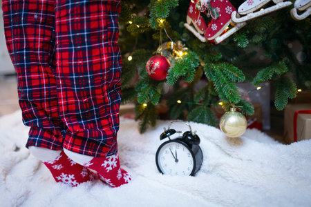 A girl dresses up a Christmas tree, a Christmas clock under a decorated tree.A girl in red Christmas...