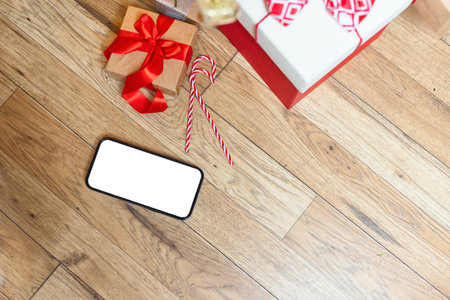 A phone with a white screen on a wooden background with gifts. Gift boxes decorated with red ribbons.Gifts for Christmas, Valentines Day, Mothers Day, Birthday. Photo with copy spaceの写真素材