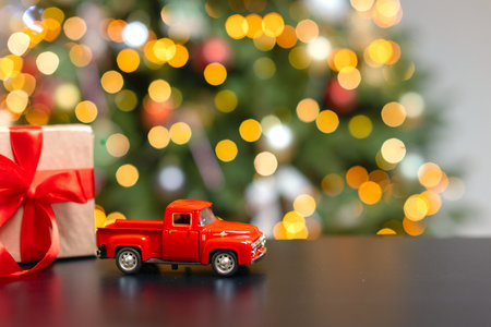 A red little car on a background of blurred Christmas lights, a gift. Christmas background with space for copy, text and advertising. Holiday banner, blurry lights and highlightsの写真素材
