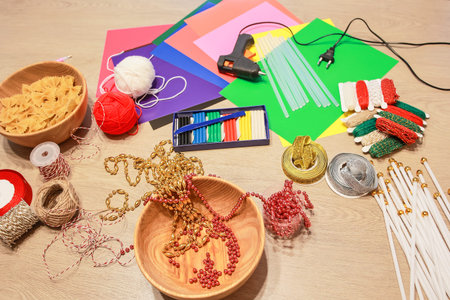 Top view composition of colorful craft supplies including yarn balls, beads, pasta, glue gun and paper sheets arranged on wooden table. Materials prepared for DIY handmade project or children creative