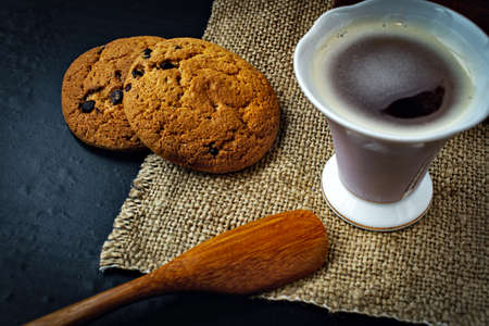 cup of coffee on fabric, cookies with chocolate and a spoon from a tree on a dark backgroundの写真素材