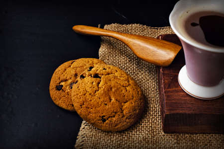 cup of coffee on fabric, cookies with chocolate and a spoon from a tree on a dark backgroundの写真素材