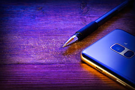 pen and blue mobile phone on a wooden backgroundの写真素材