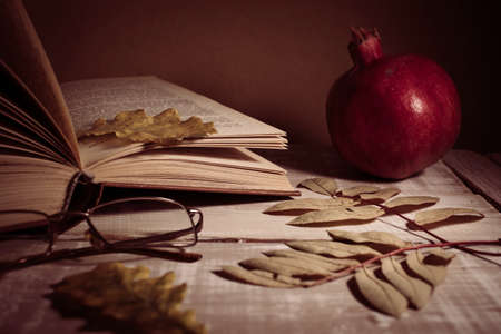Open book, glasses, pomegranate and autumn leaves on a wooden table. Autumn still life.の写真素材