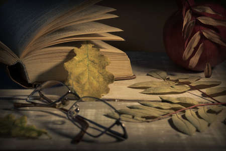 Open book, glasses, pomegranate and autumn leaves on a wooden table. Autumn still life.の写真素材