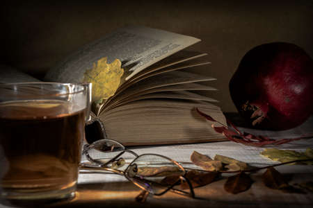 Open book, tea, glasses, pomegranate and autumn leaves on a wooden table. Autumn still life.の写真素材