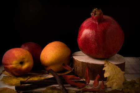 Autumn still life with pomegranate, nectarines and fallen leaves on a wooden backgroundの写真素材