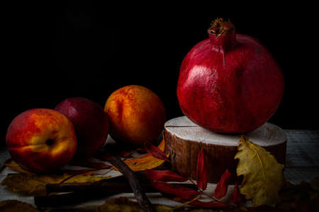 Autumn still life with pomegranate, nectarines and fallen leaves on a wooden backgroundの写真素材