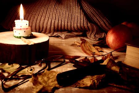Book, glasses, fruits, a burning candle and autumn leaves on a wooden table. Autumn still life.の写真素材