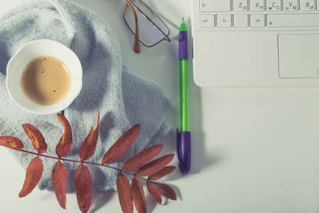 A cup of coffee with foam, a white laptop, a scarf, glasses, a pen and autumn leaves on a white background. Autumn mood.の写真素材