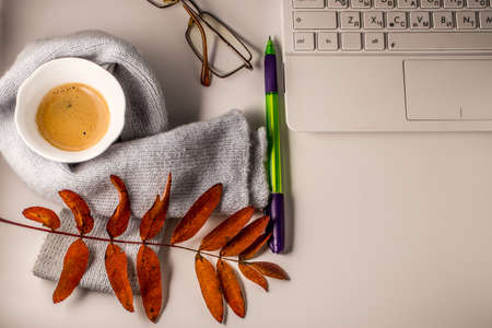 A cup of coffee with foam, a white laptop, a scarf, glasses, a pen and autumn leaves on a white background. Autumn mood.の写真素材