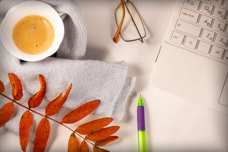 A cup of coffee with foam, a white laptop, a scarf, glasses, a pen and autumn leaves on a white background. Autumn mood.の写真素材