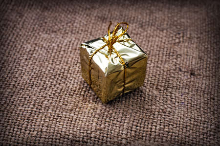 Gold gift box with gold thread on a background of rough fabricの写真素材