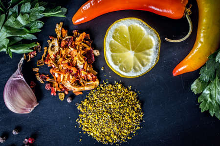 Background with red and yellow chili peppers, half a lemon, spices, garlic and parsley on a black surfaceの写真素材