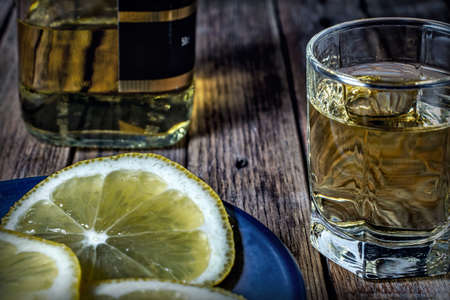 Background with a bottle of whiskey filled with a stack and sliced lemon on a wooden surface.の写真素材