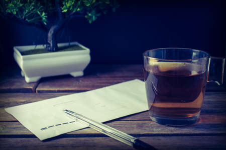 cup of hot tea, postal envelope, bonsai and pen on a wooden surfaceの写真素材