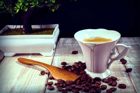 cup of coffee, spoon, coffee beans on a wooden table with bonsaiの写真素材