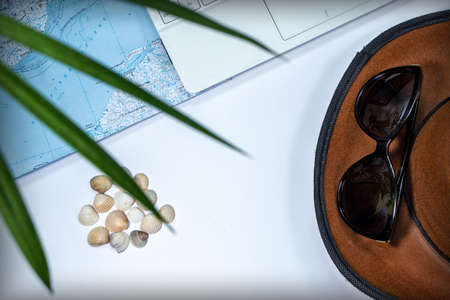 White laptop, map, seashells, hat and sun glasses on a white background. Top view through palm leavesの写真素材