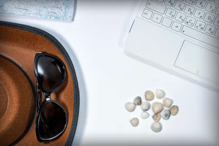 White laptop, map, seashells, hat and sun glasses on a white background. View from above