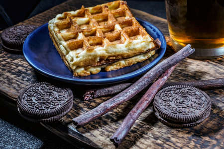 Background with Viennese waffles, chocolate chip cookies and a cup of tea on a textured wooden surface.の写真素材
