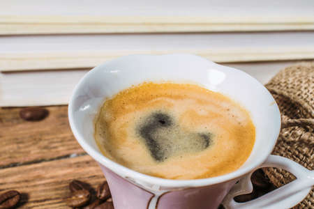 Cup of coffee with a heart painted in foam and grains scattered from a bag on a wooden tableの写真素材