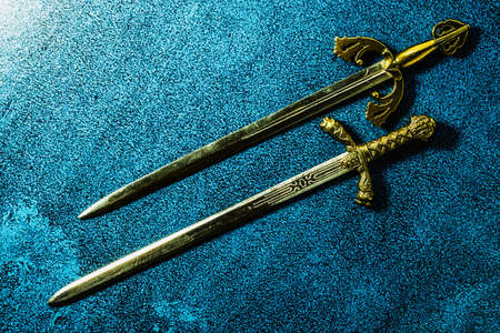 Two knightly swords lie in parallel on a dark blue background. View from aboveの写真素材
