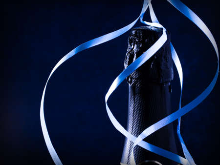 Bottle of champagne wine close-up and blue serpentine on a dark blue background. Holiday concept. Copy spaceの写真素材