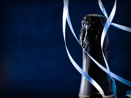 Bottle of champagne wine close-up and blue serpentine on a dark blue background. Holiday concept. Copy spaceの写真素材