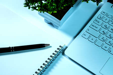 Background with a laptop, a potted plant, a spiral notebook and pen on a white table.の写真素材