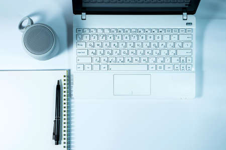 White laptop, round wireless speaker, notepad with spring binding and pen on a white background. View from aboveの写真素材