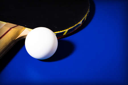 Black racket and ball for table tennis on a blue table backgroundの写真素材