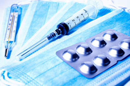Syringe for injection and silver packaging with tablets on the background of medical masksの写真素材