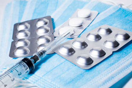 Syringe for injection and silver packaging with tablets on the background of medical masksの写真素材