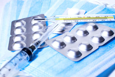 Background with medical syringe, thermometer and pills lying on medical masksの写真素材