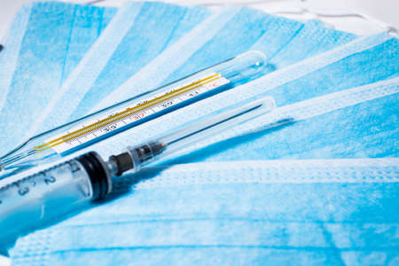 Syringe for injection and a thermometer on the background of medical masksの写真素材