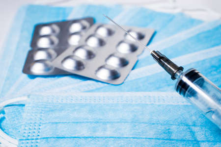 Syringe for injection and silver packaging with tablets on the background of medical masksの写真素材