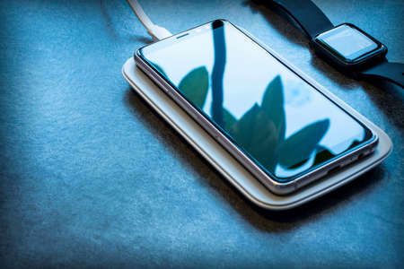 Background with a smart watch, a wireless charger and a smartphone on the screen of which the leaves...
