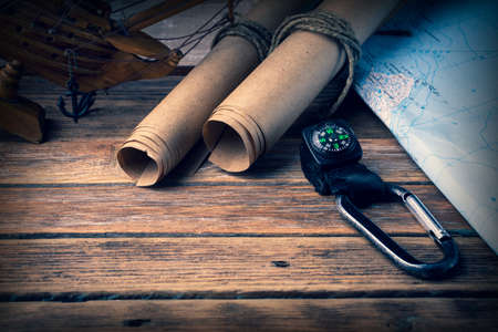 Magnetic compass, paper scrolls, geographic map and sailboat on a wooden backgroundの写真素材