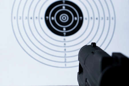Background with a pistol aimed at a round target with a black centerの写真素材