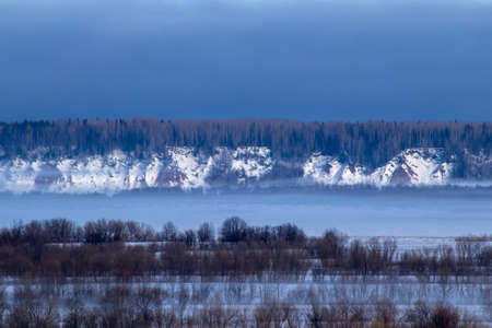winter landscape with trees and fog over a frozen riverの写真素材
