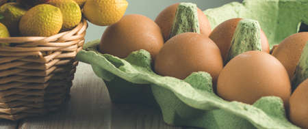 Chicken eggs in an open cardboard a box and wicker fruit basket close-up on a wooden table. Easter...