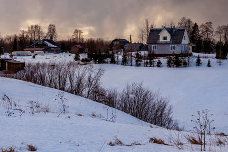 Beautiful winter landscape with a small village on a hill against the backdrop of a sunny sunset in the cloudy sky. Russia, Arkhangelsk regionの写真素材