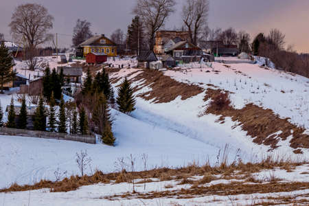 Beautiful winter landscape with a small village on a hill against the backdrop of a sunny sunset in the cloudy sky. Russia, Arkhangelsk regionの写真素材