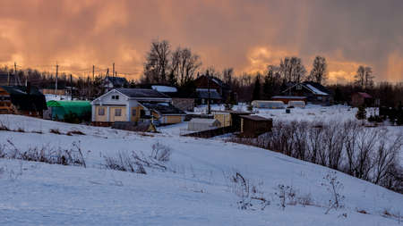 Beautiful winter landscape with a small village on a hill against the backdrop of a sunny sunset in the cloudy sky. Russia, Arkhangelsk regionの写真素材