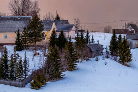 Beautiful winter landscape with a small village on a hill against the backdrop of a sunny sunset in the cloudy sky. Russia, Arkhangelsk regionの写真素材