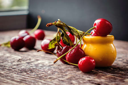 Still life with cherry berries and a yellow clay pot on an old wooden texture surface