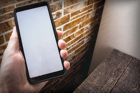 A smartphone with a white blank screen lies in a hand against the background of a home interior. Copy spaceの写真素材