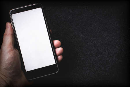 A smartphone with a white blank screen lies in a hand on a dark background. Copy spaceの写真素材