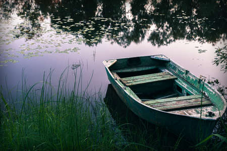 Tranquil morning landscape with river bank and old fishing boat at sunrise