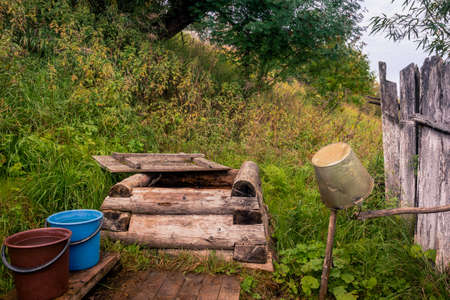 Rural retro landscape with wooden well and buckets of water on a hillside with green grassの写真素材